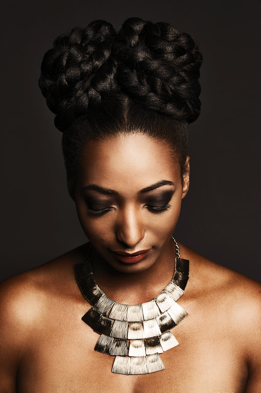 black model, modelling hair that is up an style in two plaited bunches. Her eyes are looking down.