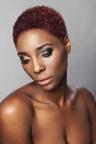 Black model, modelling her hair which is cropped very short and coloured burgundy.