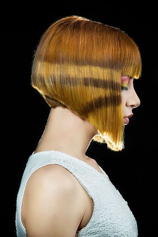 White model that is modelling hair. She is in side on profile and looking at the floor. Her hair is an angeled bob with fringe.