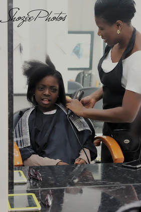 The owner of the salon with a young girl sitting in the chair getting her hair tonged.
