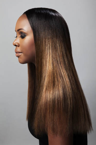 Black femal model, modelling her hair which is straight and pass her shoulders. Her hair has been highlighted different shades of brown and gold.
